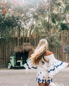 a woman is walking down the street with her hair blowing in the wind while wearing a white and blue dress