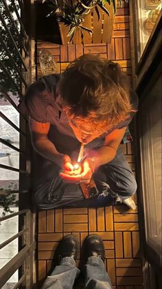 a man sitting on the ground holding a lit candle in his hand and looking down at it