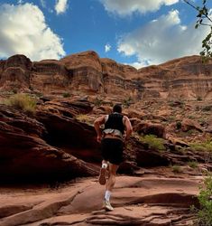 a man is running down a trail in the desert with mountains and rocks behind him