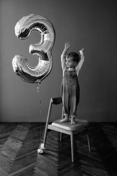 a little boy sitting on top of a chair next to two balloons in the shape of numbers