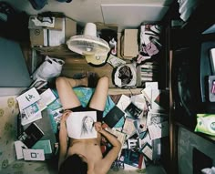 a person laying on the floor surrounded by clutter and books in a messy room