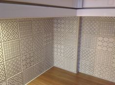 the corner of a room with decorative tiles on the wall and wood flooring in front of it