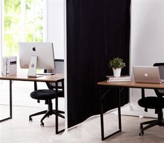 two desks with computers on them in front of a black screen divider and windows