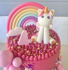 a birthday cake decorated with pink icing, rainbows and unicorn figurines