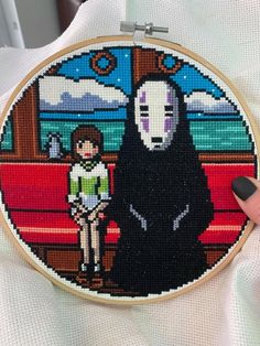 someone is holding up a cross - stitch art piece with a person in the background