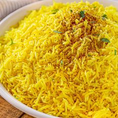 a white bowl filled with yellow rice on top of a wooden table