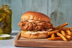 a fried chicken sandwich and french fries on a wooden cutting board with pickles next to it