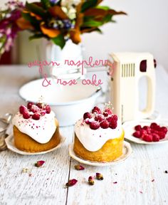 two small cakes with raspberries on them sitting on plates next to a mixer