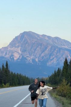 a man and woman running down the road in front of a mountain with snow on it