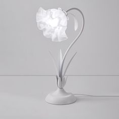 a white flower lamp sitting on top of a table next to a gray wall and floor