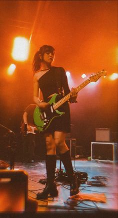 a woman standing on stage with a guitar in her hand and wearing knee high boots