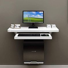 a computer desk with a monitor, keyboard and mouse sitting on it in front of a gray wall