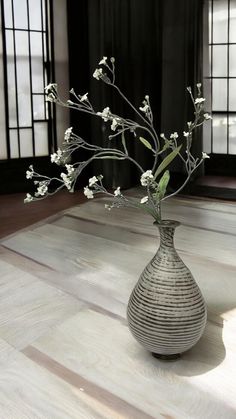 a vase filled with white flowers sitting on top of a wooden floor next to windows