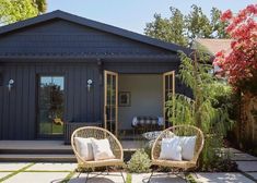 two wicker chairs sitting in front of a blue house with white pillows on them