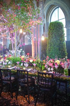 a long table with chairs and flowers on it in front of an arched window at night