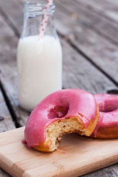 a half eaten doughnut sitting on top of a wooden cutting board next to a glass of milk