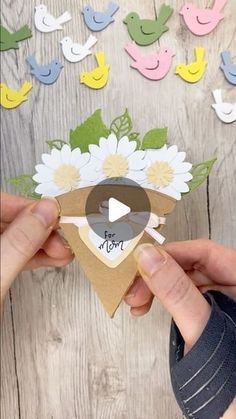 someone holding up a piece of paper with flowers and birds on it in front of a wooden background