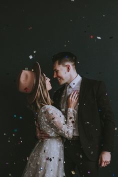 a man and woman standing next to each other in front of confetti falling from the sky