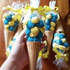 three cones with blue and yellow icing are being held by someone's hand