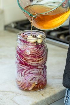 a person pouring liquid into a jar filled with onions