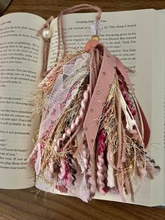 an open book with pink and white ribbons hanging from it's pages on a wooden table