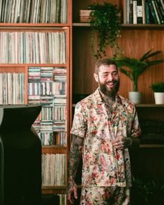 a man with tattoos standing in front of a record player and bookshelf full of records