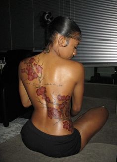 a woman sitting on the floor with her back to the camera and tattoos on her body