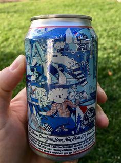 a person holding up a can of beer in front of some green grass and trees