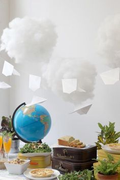 a table topped with lots of food next to a blue globe and clouds above it