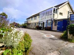 an empty parking lot in front of a building with lots of windows and flowers growing on the ground