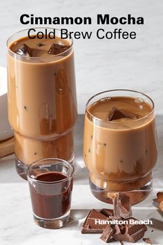 two glasses filled with cold beverages sitting on top of a white counter next to pieces of chocolate