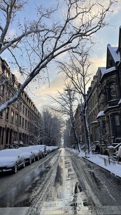 a snowy street lined with parked cars and tall buildings