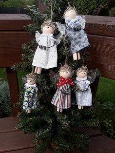 four angel ornaments hanging from a tree on a bench in front of some bushes and trees