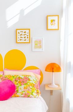 a white bed topped with lots of pillows next to a lamp and pictures on the wall