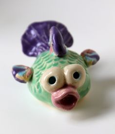 a ceramic figurine of a green fish with purple ears and tail sitting on a white surface