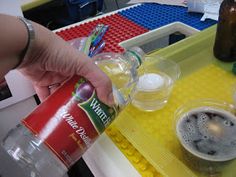 a person pouring something into a cup on top of a lego table with other items