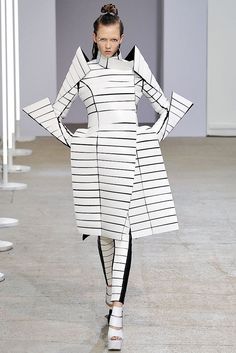 a model walks down the runway in a white and black striped dress with long sleeves