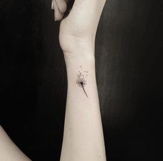 a woman's wrist with a dandelion tattoo on the left side of her arm