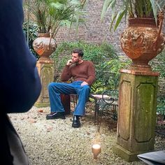 a man sitting in a chair next to two large planters and a small table