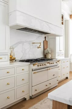 a kitchen with white cabinets and gold pulls on the stove top, along with marble counter tops