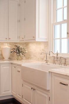 a kitchen with white cabinets and marble counter tops is pictured in this image, there are flowers on the window sill