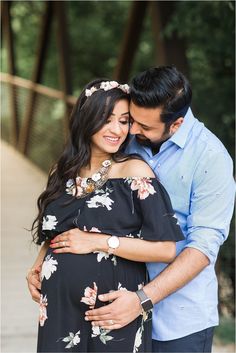 a pregnant woman hugging her husband while standing in front of a bridge