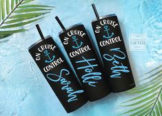 three black tumblers with white writing on them sitting next to palm leaves and water