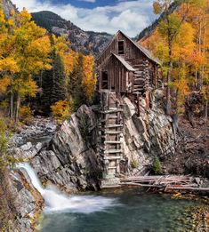 an old water mill in the mountains surrounded by fall foliage and trees with yellow leaves