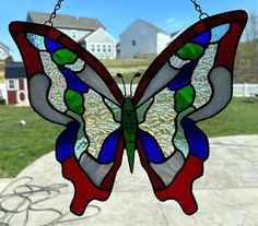 a stained glass butterfly hanging from a chain in front of a house on a sunny day