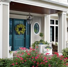 the front porch is decorated with flowers and potted plants, along with a wreath on the door