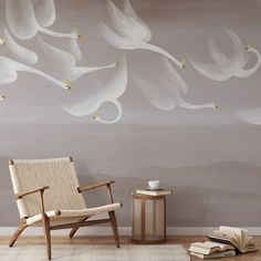 a chair sitting in front of a wall with white flowers painted on it and an open book next to it