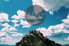 a group of people standing on top of a mountain under a blue sky with clouds