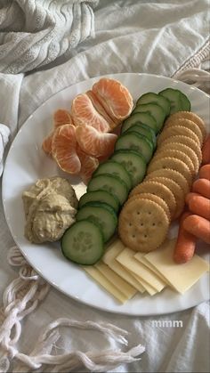 a white plate topped with crackers, cucumbers and oranges