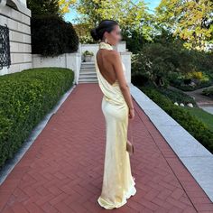 a woman in a yellow dress standing on a brick walkway next to bushes and trees